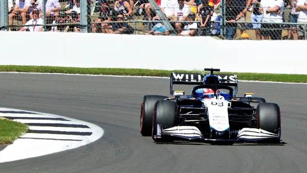 Carro de Fórmula 1 em alta velocidade em curva rápida, com foco no cockpit e cintos de segurança visíveis