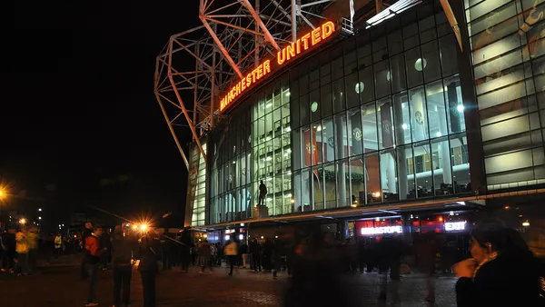 Banco de reservas vazio de um estádio de futebol inglês com gramado iluminado ao fundo