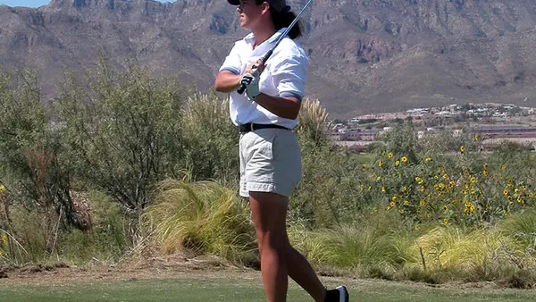 Jogador de golfe durante taco de saída em campo aberto, com bandeira ao fundo